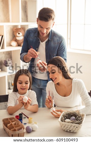 Charming little girl and her beautiful young parents are painting Easter eggs and smiling