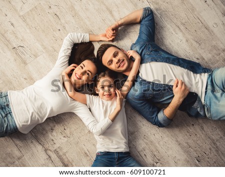 Top view of cute little girl and her beautiful young parents looking at camera and smiling while lying on the floor at home Royalty-Free Stock Photo #609100721