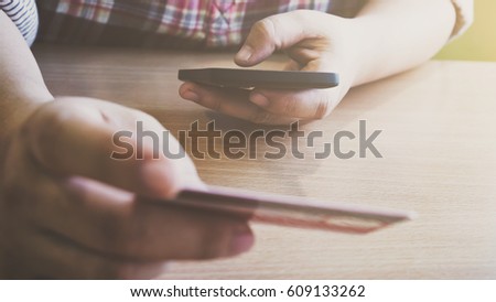 Using laptop and mobile phone to online shopping and pay by credit card. This picture is focus at woman's hand and use warm bright sunlight filter for feeling comfortable.