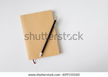 Top view of closed blank craft paper cover notebook with pencil on white desk background