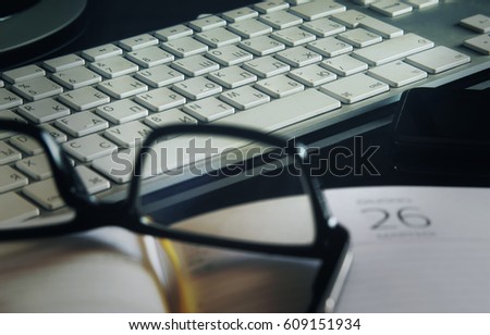The keypad of the computer of white color on a background. The foreground - a notepad and glasses in a black casing - not in sharpness. Normal contrast. Horizontal format. Indoors. Color. Photo.