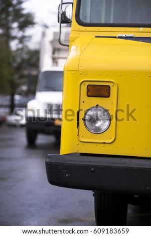 A part of old style bright yellow little buggy truck with a covered trailer box for transporting small loads and delivering goods to local stores and companies rides down the street of a urban city