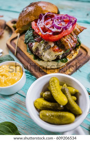 Tasty burger with beef with spinach and gherkin served on a small board on a wooden background.