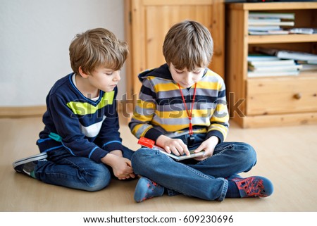 Two little kid boys reading a book at home. Older schoolboy reading for his brother, preschool sibling a fairytale or story. Family, children, education and leisure.