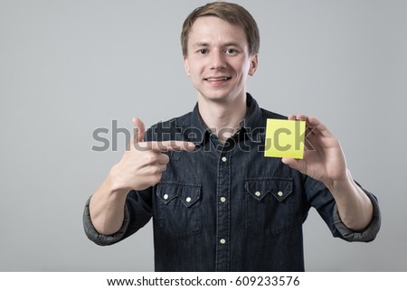 Young man showing yellow empty office sticker on grey background