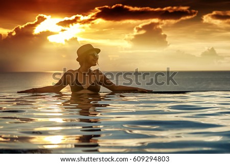 Young woman relaxing on the swimming pool, near the sea in the sunset