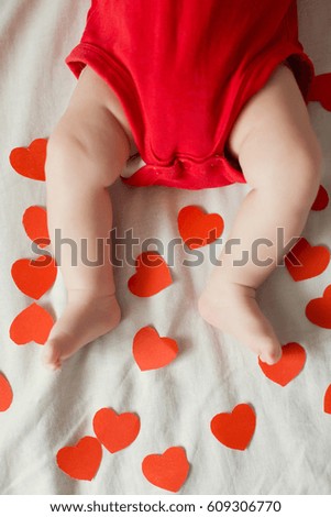 cute baby feet near red paper hearts