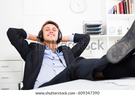 Portrait of young positive relaxed man in formal wear listening music in office