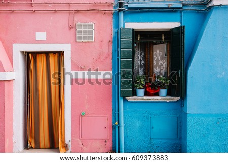 Beautiful colorful house facade on Burano island, north Italy. Half pink and half blue house wall with a door and a window with flowers on it
