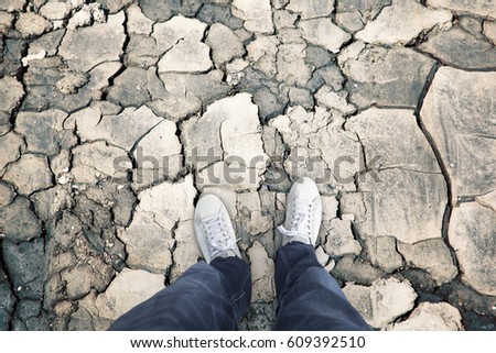 Person standing on the dried cracked earth soil ground. Personal perspective used.