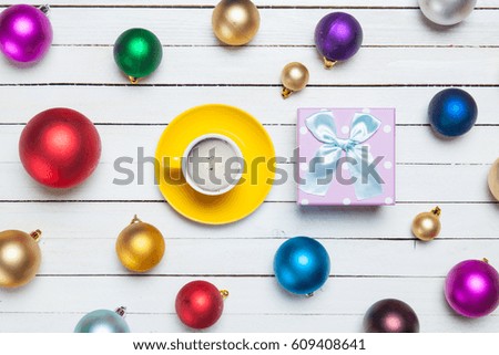 photo of yellow cup of coffee and cute gift near colorful baubles on the wonderful white wooden background