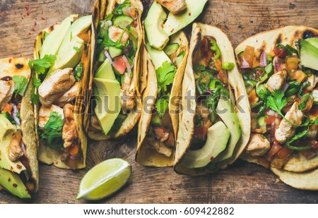 Tacos with grilled chicken, avocado, fresh salsa sauce and limes over rustic wooden background, top view. Healthy low carb and low fat lunch or food for company. Dieting and weight loss concept