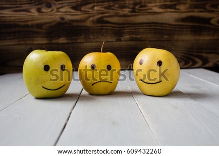 yellow apples with drawn emotions on wooden background