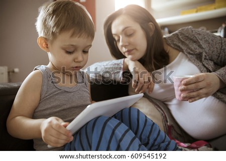 Pregnant Woman Drinking Coffee While Watching Her Son Playing On The Tablet