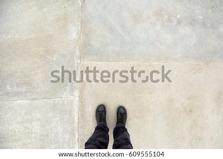 Man standing on concrete flooring surface, feet in leather winter shoes from above, copy space for quotation or graphic