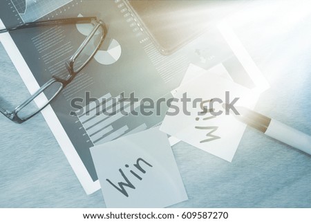 Win written on sticky note with marker spectacles and graph on wooden table