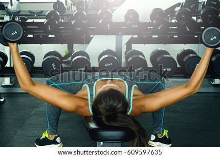 Young and beautiful woman working out with dumbbells in gym Royalty-Free Stock Photo #609597635