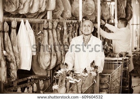 Mature butcher and his young assistant with jamon joints at meat factory