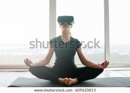 A young beautiful girl in virtual reality glasses makes yoga and aerobics remotely. Future technology concept. Modern imaging technology. Classes in single sports remotely. Royalty-Free Stock Photo #609620813
