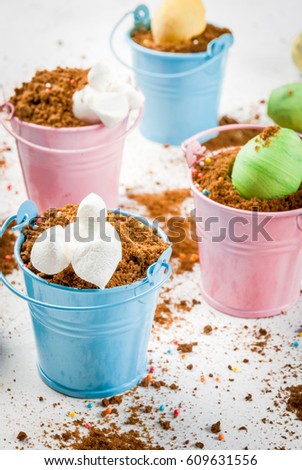 Funny baby food for easter, decorating table. Dessert of chocolate cookies in colored decorative buckets, with colorful chocolate eggs and marshmallow bunnies diving into holes. copy space 