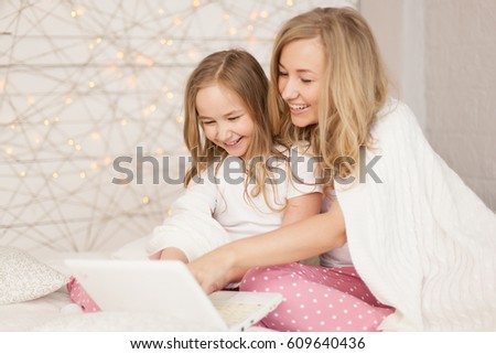 Mother and daughter sit on bed in pajamas and have fun, use laptop. Lifestyle. Happy family. Education, learn