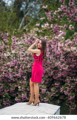 Beautiful girl posing to the photographer against the background of blooming pink trees. Spring. Sakura.
