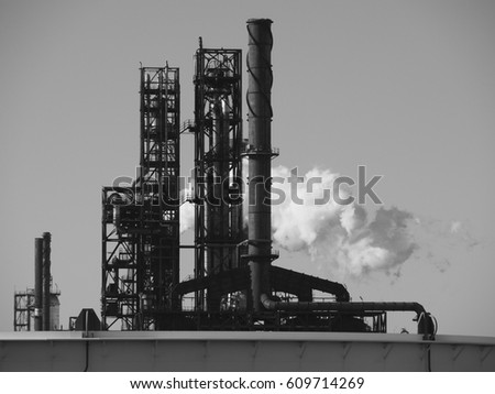A monochrome photograph of the outlets and metal pipes of a refinery.