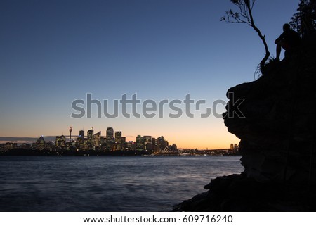 Silhouette of man overlooking Sydney city landscape and harbour bridge at sunset with blurred water