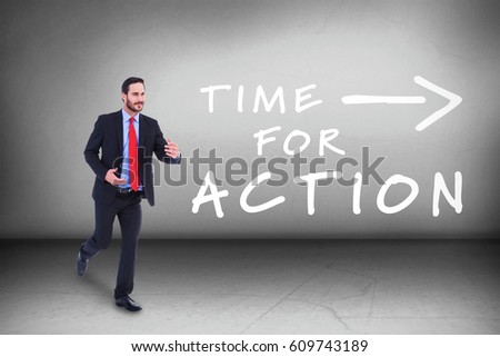 Smiling young businessman in suit running against grey room