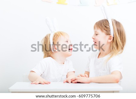 two small cute blond kids in preschool age sitting together indoors and looking direct to camera. children wearing easter rabbit ears together