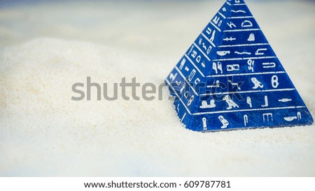 Abstract blue pyramid with hieroglyph staying on sand