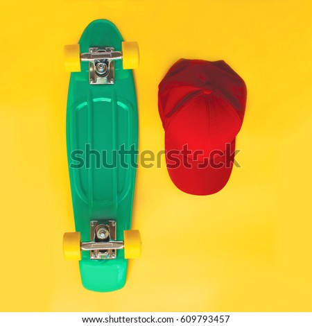 Fashion set. Skateboard and baseball cap over yellow background, top view. Vintage hipster colorful photo. Flat lay
