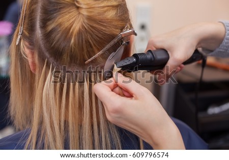 The hairdresser does hair extensions to a young girl, a blonde in a beauty salon. Professional hair care. Royalty-Free Stock Photo #609796574