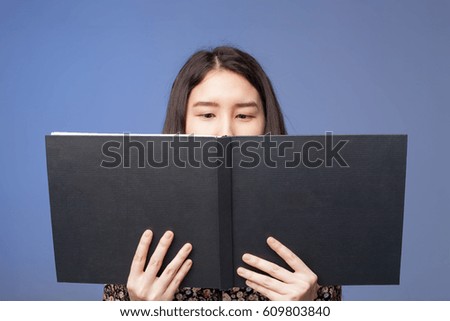 An asian girl in a dress reading a black book in her hands. 
