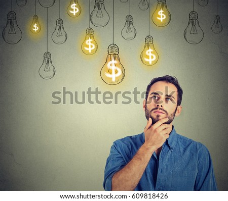 Portrait thinking handsome young man looking up at many dollar idea light bulbs above head