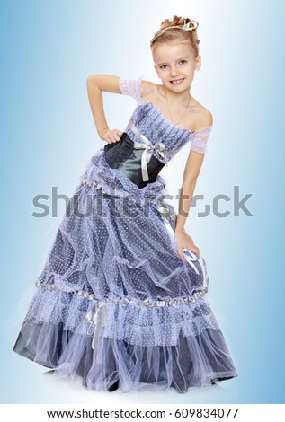 Slender little girl , with beautiful hair on his head,elegant long Princess dress.The girl twisted to the side and keeps his hand on his knee.On the pale blue background.