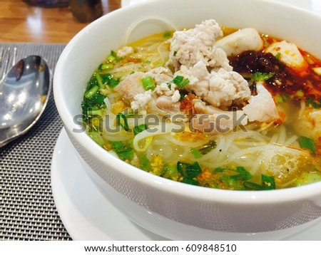 Spicy tom yum noodle with pork in white bowl.