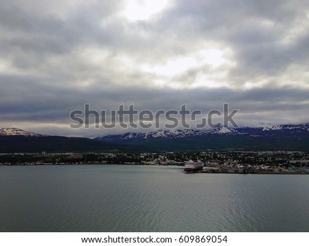Cruise ship docked in the Akureyri Iceland port on the Norwegian Sea and dusk. Traveling to Iceland in the summer in July. Calm sea  with dramatic clouds and setting sun in the sky.