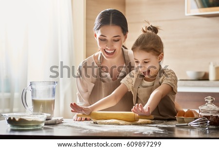 Happy loving family are preparing bakery together. Mother and child daughter girl are cooking cookies and having fun in the kitchen. Homemade food and little helper.