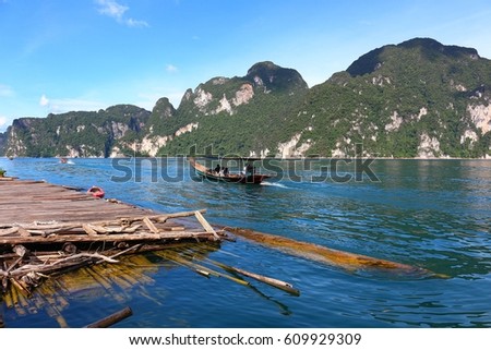 Khaosok or Ratchaprapa Dam in Southern of Thailand. The mountain and blue sky in background with bamboo raft and a tourist boat in the clear water. This photo took in July 2016.