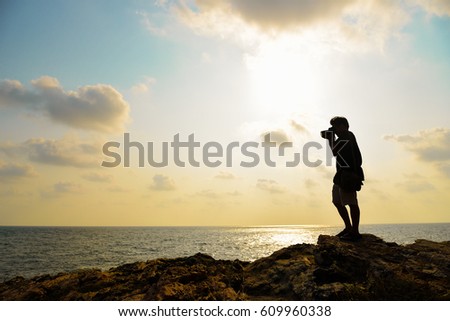 Silhouette of photographer taking photo on the top of mountaing before sunset