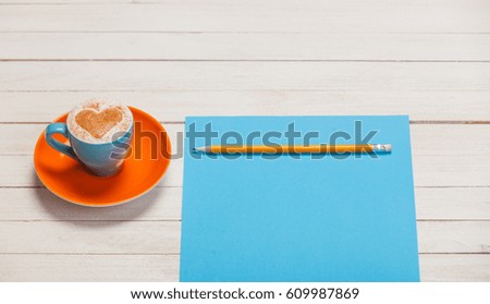photo of beautiful blue cup of coffee and sheet of paper with pencil on the wonderful white wooden background