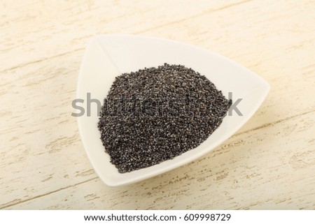 Poppy seeds in the bowl over wooden background