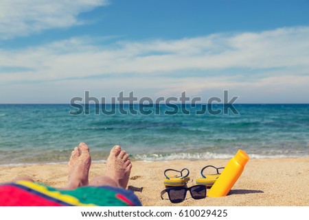 Man sunbathing on the sandy beach. Shallow depth of field on feet and flip flops.