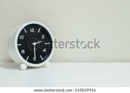 Closeup black and white alarm clock for decorate show show half past two o'clock or 2:30 p.m. on white wood desk and cream wallpaper textured background with copy space