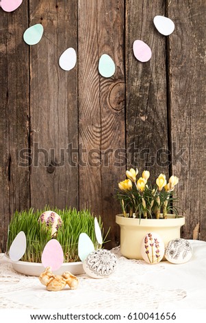 Happy Easter. Composition for greeting card: Easter eggs, yellow crocus, grass, rabbits, grass on over white lacy tablecloth on wooden background. Holiday concept. Copy space.