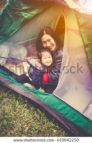 Vintage tone photo of happy asian family looking at camera on camping trip in their tent, outdoors on summer morning with bright sunlight. Mother hugging daughter and smiling happy together.