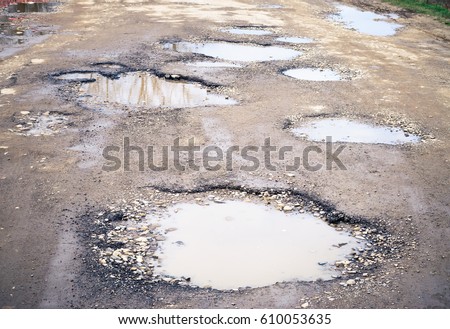 Road destroyed after winter. Puddles in the pits in the road . Royalty-Free Stock Photo #610053635