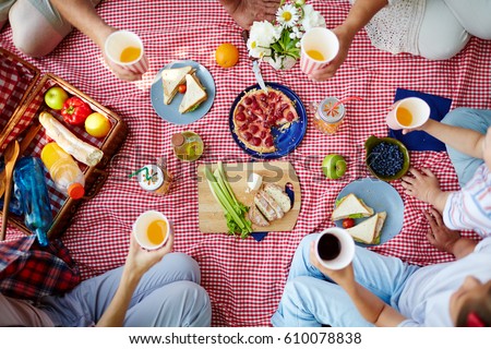 Group of humans with drinks gathered by dinner on picnic cloth Royalty-Free Stock Photo #610078838