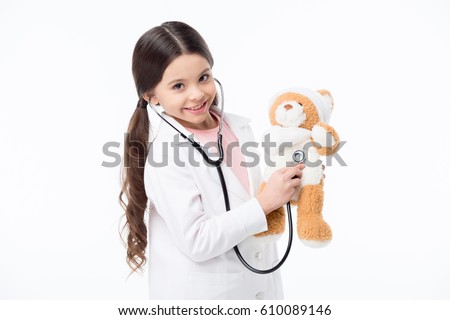 Smiling little girl playing doctor and listening teddy bear with stethoscope isolated on white Royalty-Free Stock Photo #610089146